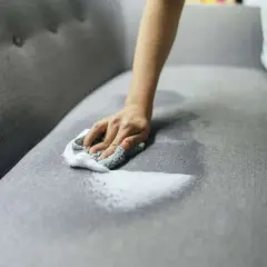 A hand with a soapy cloth gently cleans a grey couch cushion, showing how to wash couch cushion covers for a fresh look.