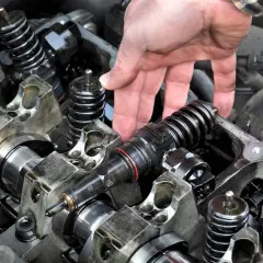 Mano manipulando un inyector de combustible para su limpieza. El motor muestra componentes mecánicos y resortes.