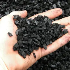 Dłoń trzyma garść czarnego, pokruszonego węgla. To ekogroszek, paliwo do nowoczesnych kotłów.
