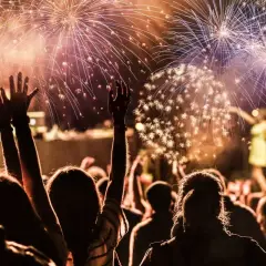 Folla festante al ritmo di canzoni di Capodanno famose, con fuochi d'artificio che illuminano il cielo.