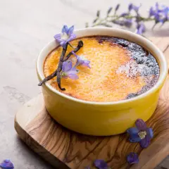 Creme brulee rezept: goldbraune Kruste, Vanilleschoten und blaue Blüten zieren das Dessert auf einem Holzbrett.