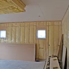 Travaux en cours pour isoler un garage non chauffé. Isolation jaune visible sur les murs et le plafond, avec des plaques de plâtre et des fenêtres.
