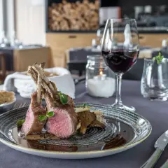 Carré d'agnello al forno con funghi e un bicchiere di vino rosso, un abbinamento perfetto per un pasto speciale.
