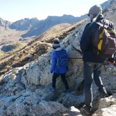 Deux randonneurs escaladent un sentier rocheux dans le cirque de Morgon, avec des montagnes escarpées en arrière-plan.