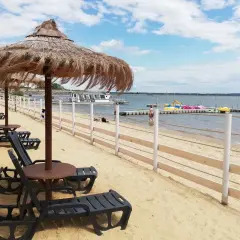 Plaża nad otmuchowskim jeziorem, leżaki pod strzechą, w oddali kolorowe rowerki wodne i statek wycieczkowy.