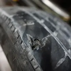 Gros plan sur une hernie sur un pneu de voiture, montrant le caoutchouc déchiré et usé. Un danger potentiel sur la route.