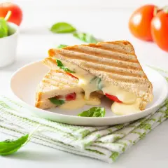 Grillowany tost z serem, pomidorami i szpinakiem na białym talerzu, obok pomidory i miseczka szpinaku.