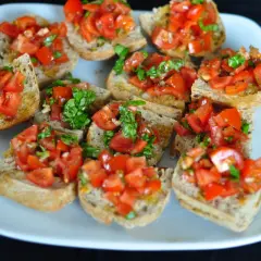 Bruschetta z pomidorami i bazylią, ułożona na białym talerzu. Chrupiące grzanki z dodatkiem świeżych, soczystych pomidorów i aromatycznej bazylii.