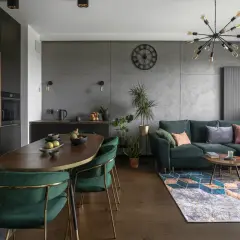 Nowoczesna kuchnia i salon z zieloną kanapą. Obok okna widać grzejnik, który można estetycznie ukryć, np. za pomocą zabudowy.