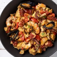 Panzanella di mare ricca con gamberi, polpo, cozze e pomodori, condita con pane raffermo. Un piatto estivo saporito.