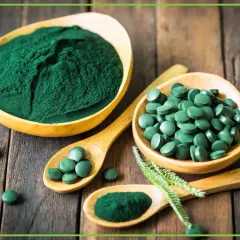 Zielona spirulina w proszku i tabletkach na drewnianym tle. Dowiedz się, spirulina co to jest i jakie ma właściwości.