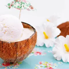 Delicioso helado de coco servido en su cáscara, adornado con una sombrilla tropical y flores blancas.