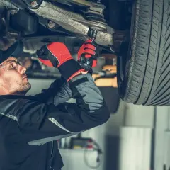 Mechanik dokręca sworzeń w zawieszeniu auta, pracując pod podniesionym pojazdem.