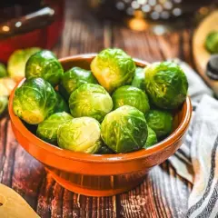 Frischer Rosenkohl in einer Schale, bereit für leckere Rosenkohl Rezepte. Ein Holzlöffel und ein Küchentuch liegen daneben.