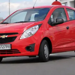 Czerwony Chevrolet Spark na drodze. Kierowca w środku. Wiele osób szuka chevrolet spark opinie przed zakupem.