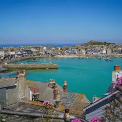 En solig vy över St Ives med turkost vatten, båtar och hus. Blommor i förgrunden ger en somrig känsla.