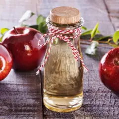 Rote Äpfel und eine Flasche Apfelessig auf Holz. Die natürliche Apfelessig Wirkung auf die Haut ist ein Geheimnis der Schönheit.