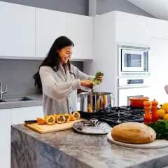 Uśmiechnięta kobieta gotuje w nowoczesnej kuchni. Na blacie leżą cytryny, pomarańcze i chleb. Czas od zjedzenia do wydalenia zależy od wielu czynników.