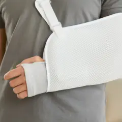 Osoba w szarym t-shircie nosi biały temblak na rękę. Czy trzeba nosić cały czas temblak? To pytanie zadaje sobie wielu po urazie.