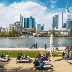 Frankfurt Geheimtipps: Menschen genießen das Leben am Mainufer mit Blick auf die Skyline. Ein perfekter Ort zum Entspannen und Beobachten.