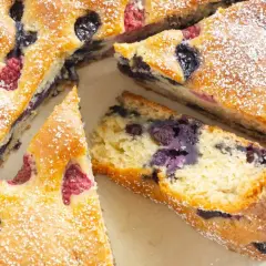 Saftiger, veganer Kuchen mit Blaubeeren und Himbeeren, bestäubt mit Puderzucker. Ein Genuss für alle!