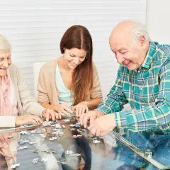 Trois personnes, deux aînées et une jeune femme, s'amusent à assembler un puzzle, une activité stimulante pour les jeux de mémoire.