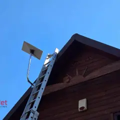 Antena satelitarna Starlink zamontowana na dachu drewnianego domu. Obok drabina, gotowa do pracy.