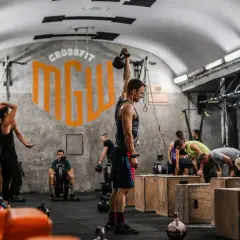 Ludzie ćwiczący CrossFit w siłowni, jeden mężczyzna podnosi kettlebell.