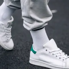 Białe sneakersy z zielonym akcentem na pięcie, na ciemnym tle. Dowiedz się, jak pozbyć się zagięć na butach, by wyglądały jak nowe.