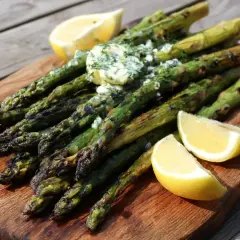 Grilla sparris med smör och dill, serverad med citronklyftor på en träskärbräda. Perfekt sommarbuffé!