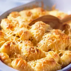Un plat de gratin de gnocchi doré et gratiné au fromage, prêt à être servi avec une cuillère en bois.