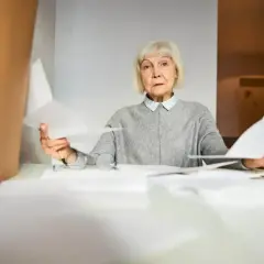 Zmartwiona starsza pani z dokumentami w rękach zastanawia się, czy renta wlicza się do emerytury.