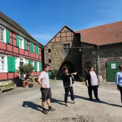 Vier Personen stehen vor einem historischen Fachwerkhaus und einem steinernen Torbogen auf dem Gut Nesselrath.