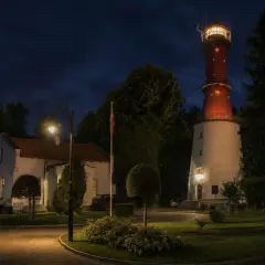 Nocna panorama latarni morskiej Rozewie. W oddali widać charakterystyczną czerwoną wieżę, a bliżej białe budynki i ceglany komin.