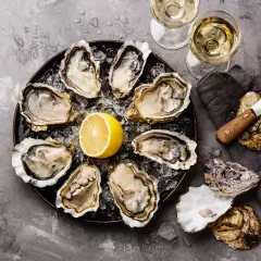 Plateau d'huîtres fraîches avec citron, deux verres de vin blanc, parfait pour le meilleur vin blanc pour fruits de mer.