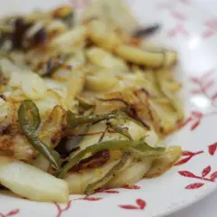 Plato de patatas panaderas al horno con cebolla y pimientos verdes, recién sacadas del horno y listas para disfrutar.