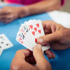 Hände halten Spielkarten, ein Spiel zur Förderung der kognitiven Fähigkeiten bei Demenz.