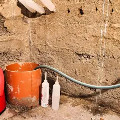 Rote Tauchpumpe mit Schlauch und Rohr zur Vorbereitung des Grundwasser abpumpen. Zwei leere Flaschen stehen daneben.