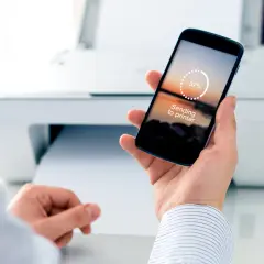 Mężczyzna trzyma smartfon z napisem "Sending to printer", pokazując, jak wydrukować z telefonu przez wifi.