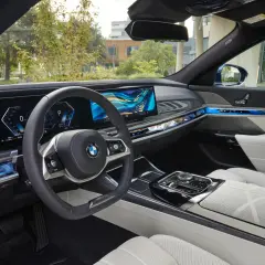 Wnętrze BMW 740d z nowoczesnym panelem cyfrowym, podświetlanymi detalami i komfortowymi, białymi fotelami.
