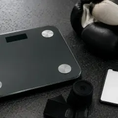 Boxing gloves, hand wraps, a scale, and a smartphone are laid out, ready for an amateur boxer to check their weight for the correct amatuer boxing weight classes.