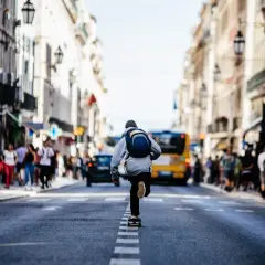Chłopak na deskorolce przemierza ruchliwą ulicę w ramach miejskiej fotografii. W tle widać ludzi i żółty autobus.
