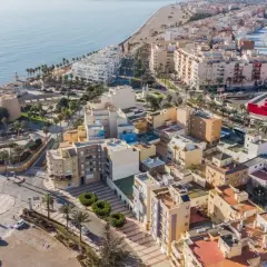 Vista aérea del **centro de Roquetas de Mar**, con el castillo, la playa, edificios residenciales y el mar Mediterráneo.