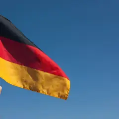 Ręka trzyma flagę Niemiec na tle błękitnego nieba. Chcesz wiedzieć, jak zaadresować list do Niemiec?
