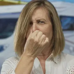 Frau hält sich die Nase wegen modrigem Geruch vor einem Wohnmobil.