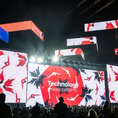 Wielkie ekrany na scenie pokazują ludzi w czerwonych strojach, tworzących wzory. To inspiracja, jak zarabiać na zdjęciach, wykorzystując kreatywność i technologię.