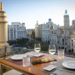 Una mesa en una terraza con vistas a la ciudad, con copas de vino y aperitivos, bajo el cielo de Atenea.
