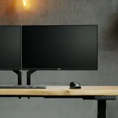Dwa monitory LG na regulowanym biurku, zamontowane na uchwycie z mocowaniem **standard VESA**. Obok klawiatura i myszka.