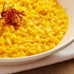 Aksamitne risotto alla milanese, złociste od szafranu, podane w białej misce, ozdobione nitkami szafranu.