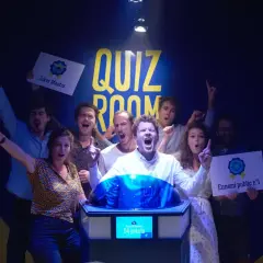 Équipe joyeuse dans une "Quiz Room" à Paris La Villette, célébrant une victoire. Ils tiennent des pancartes "Joker Master" et "Ennemi public n°1".